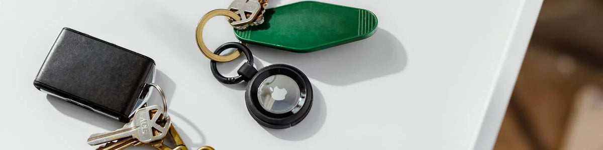 Apple AirTag in a black OtterBox holder and keys on a white table top