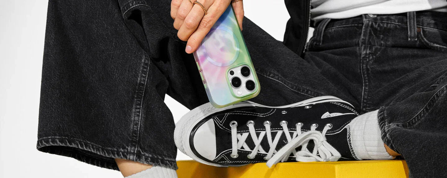 Woman wearing black jeans and shoes holding an iPhone 15 Pro in a colorful, hydro dipped OtterBox Figura Series Artist Collection phone case for iPhone 