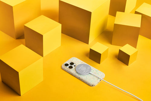 iPhone 15 in a white OtterBox Core Series phone case connected to wireless charger on yellow background