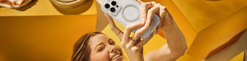 Woman taking a selfie on white iPhone 16 Pro Max in clear MagSafe OtterBox phone case on a yellow backgroung