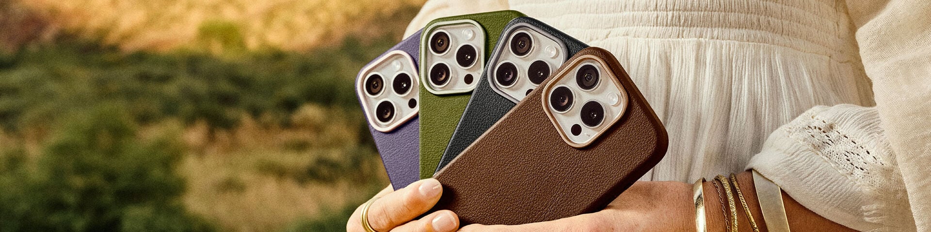Woman holding a variety of colorful OtterBox Symmetry Series Cactus Leather iPhone cases for iPhone 16 Pro on a desert background