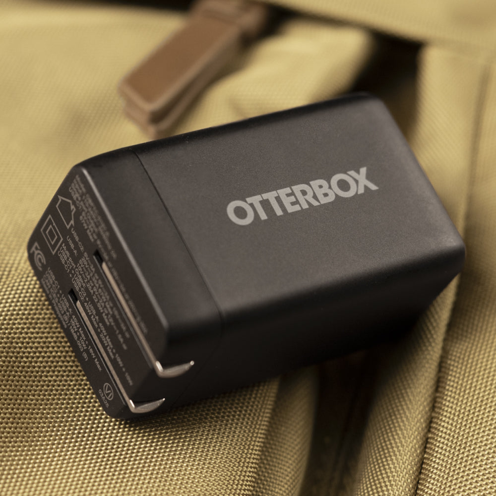 A black Otterbox electronic device with silver branding, resting on a textured khaki fabric surface.