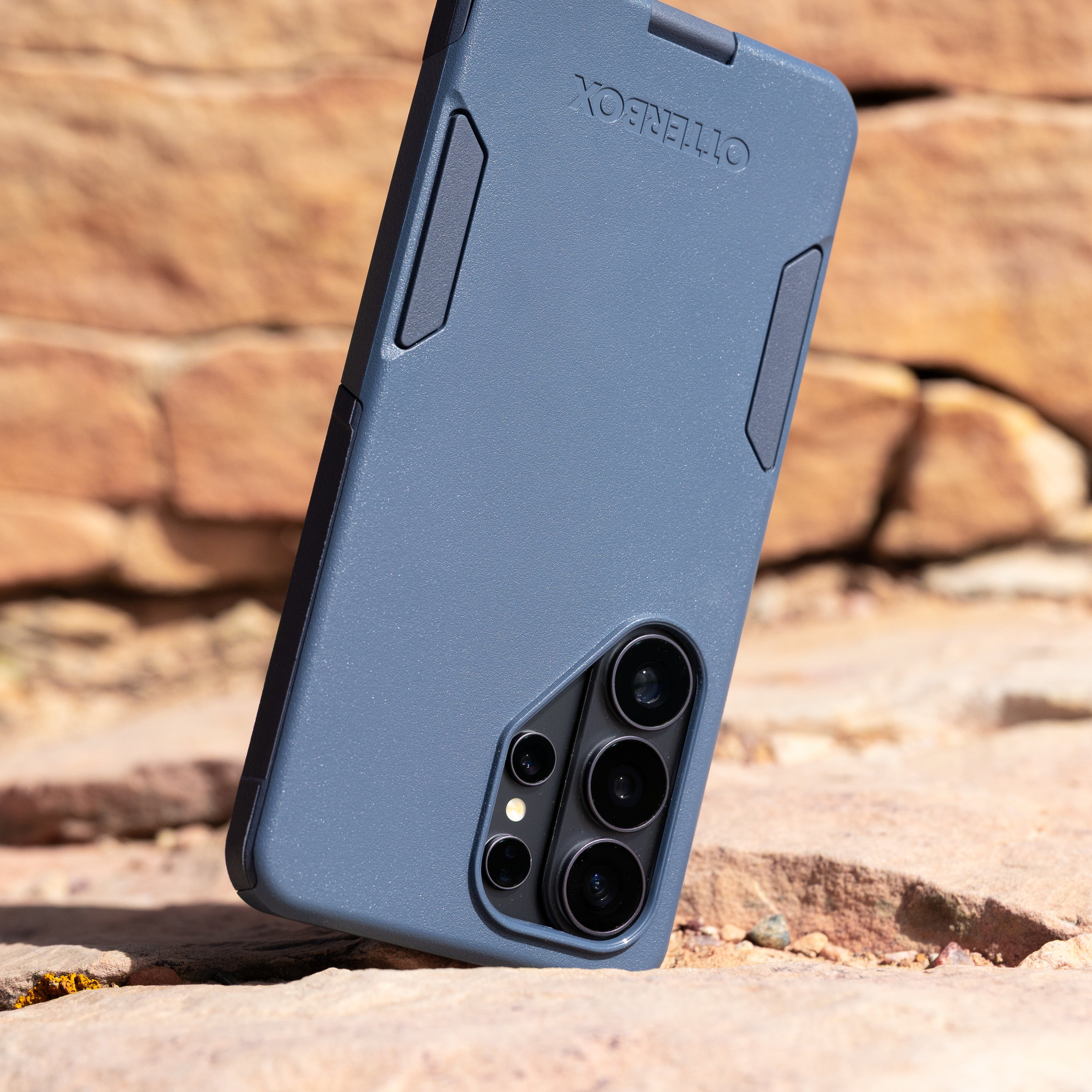 Blue phone case with 'OtterBox' branding on a rocky surface