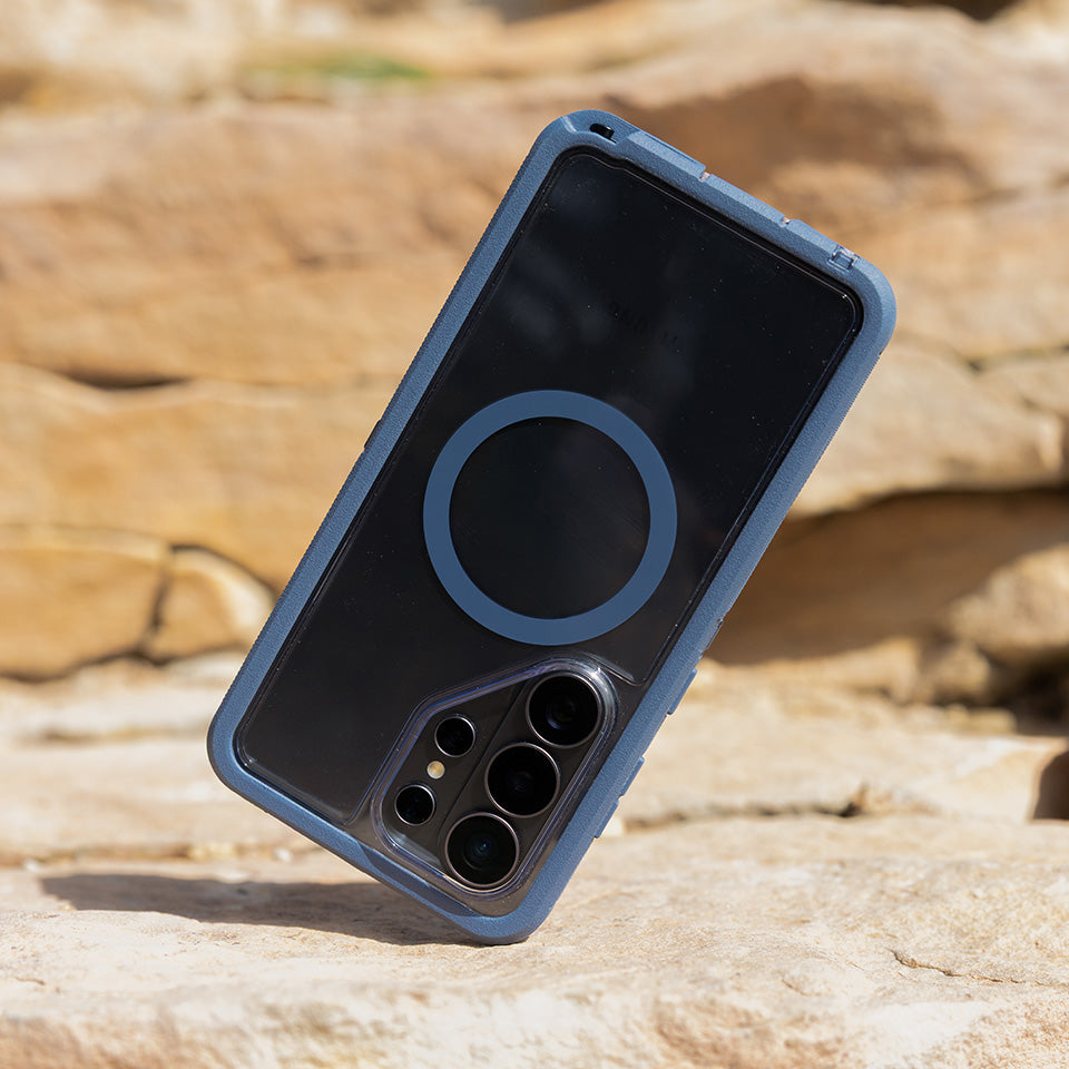 Clear Defender phone case with a blue border on a rocky surface.