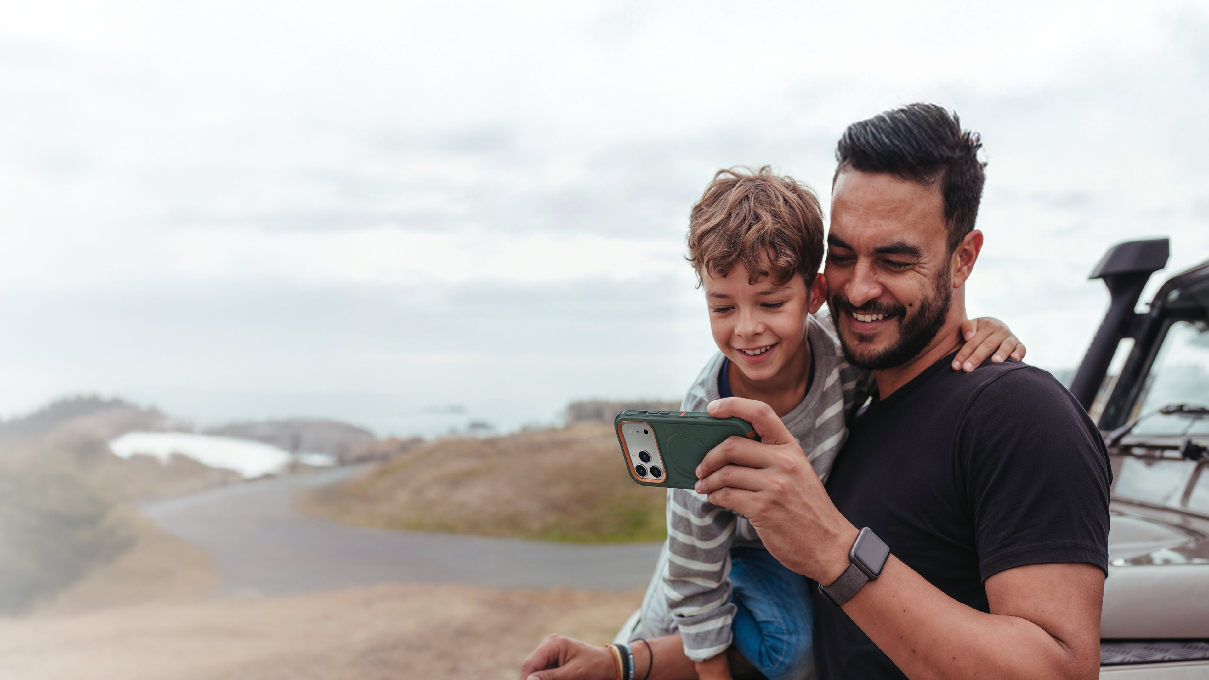 Man and child taking a selfie with a phone in a scenic outdoor setting.
