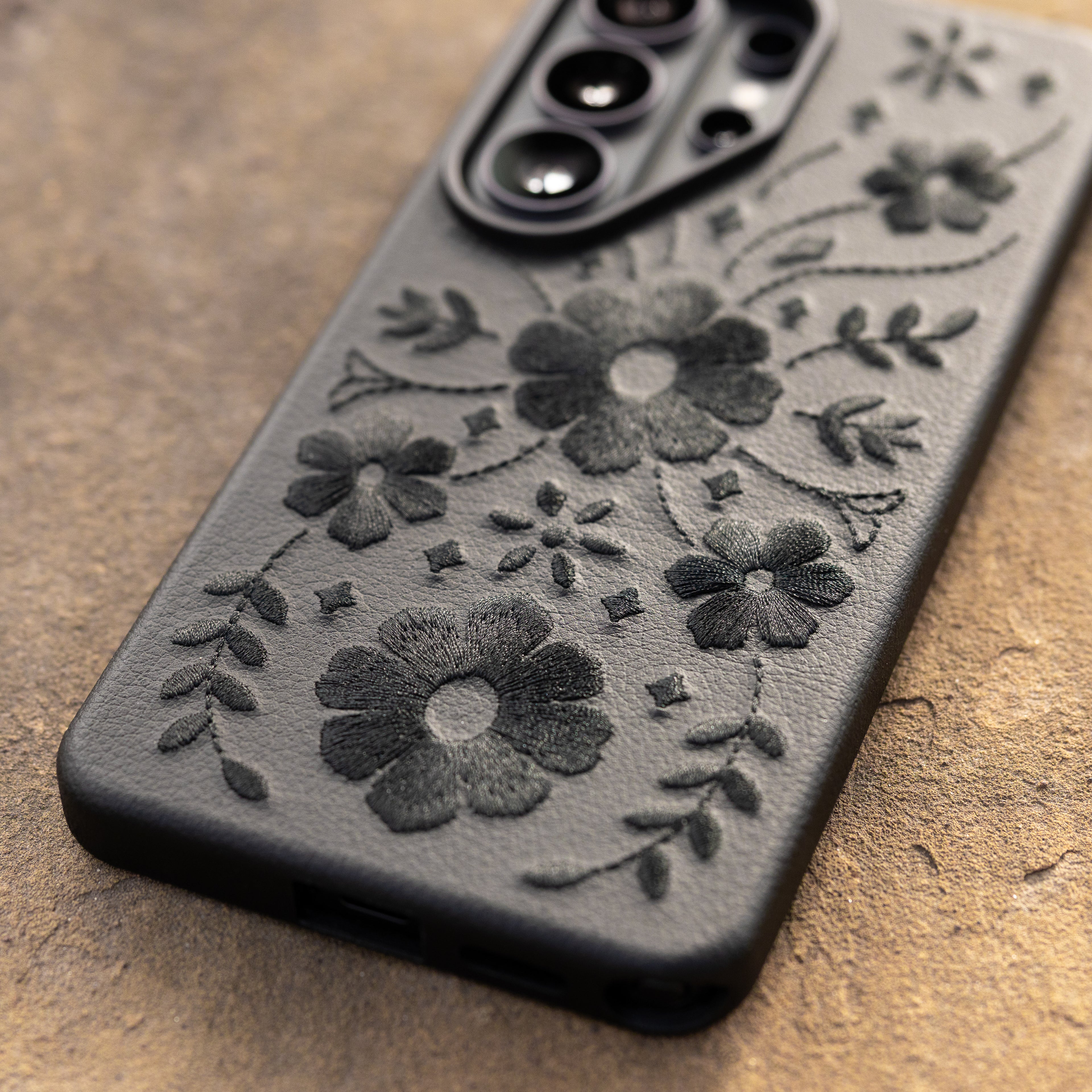 Black floral embroidered phone case on a textured surface