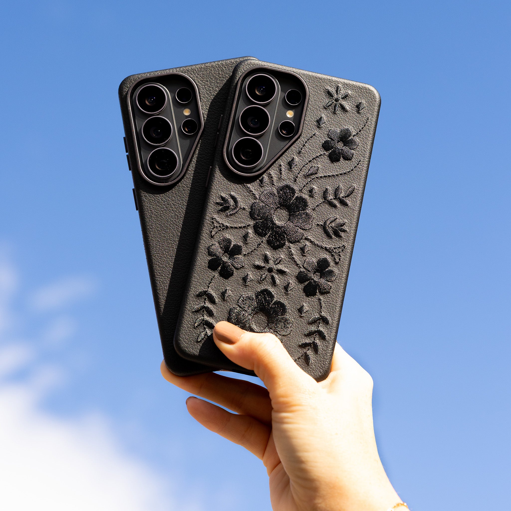 Black floral embroidered phone case held against a blue sky