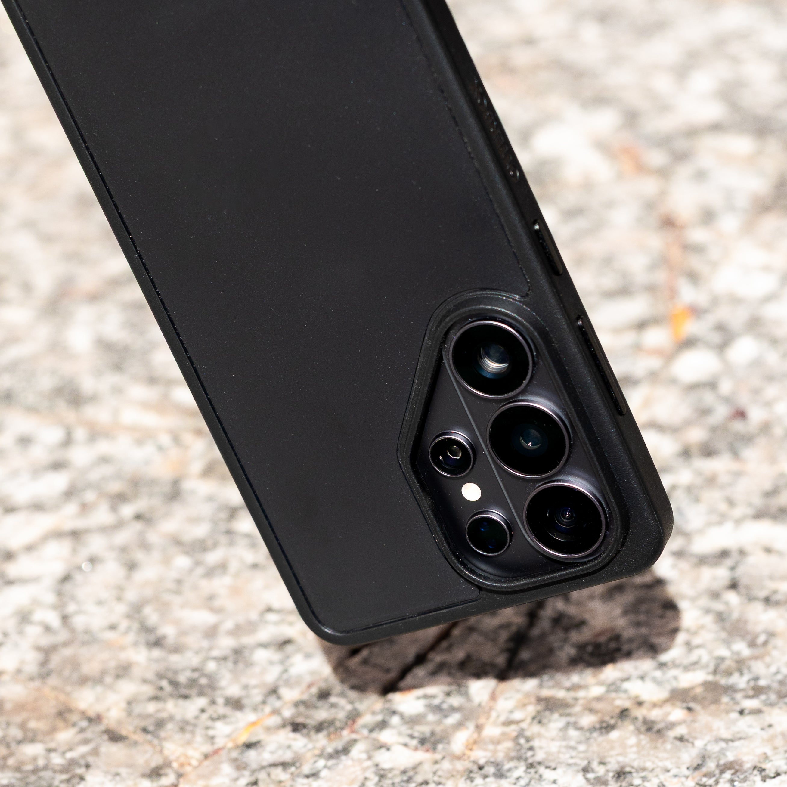 Close-up of a black phone case with camera lens on a textured surface