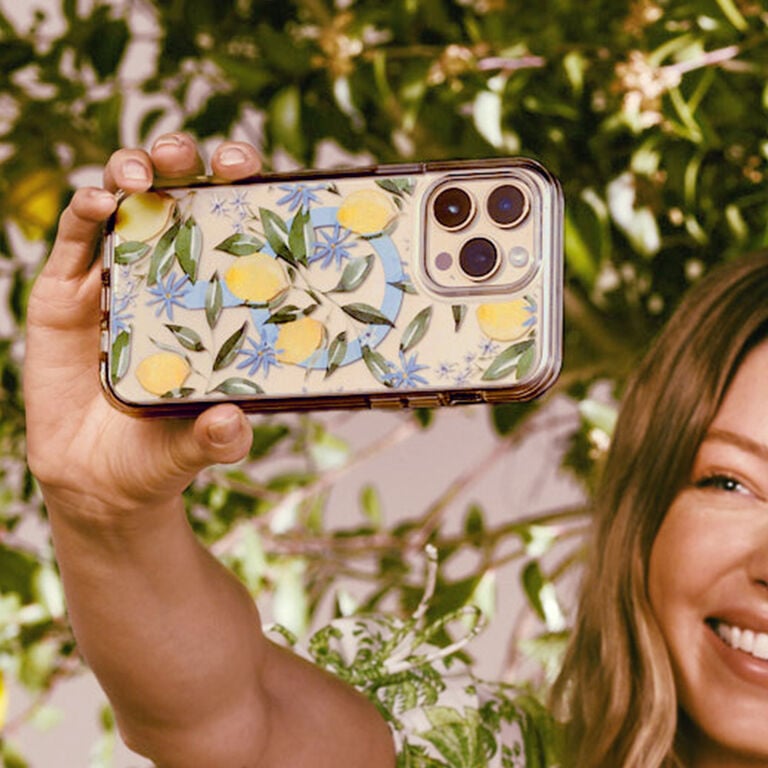 Person holding a phone with a floral case against a green leafy background