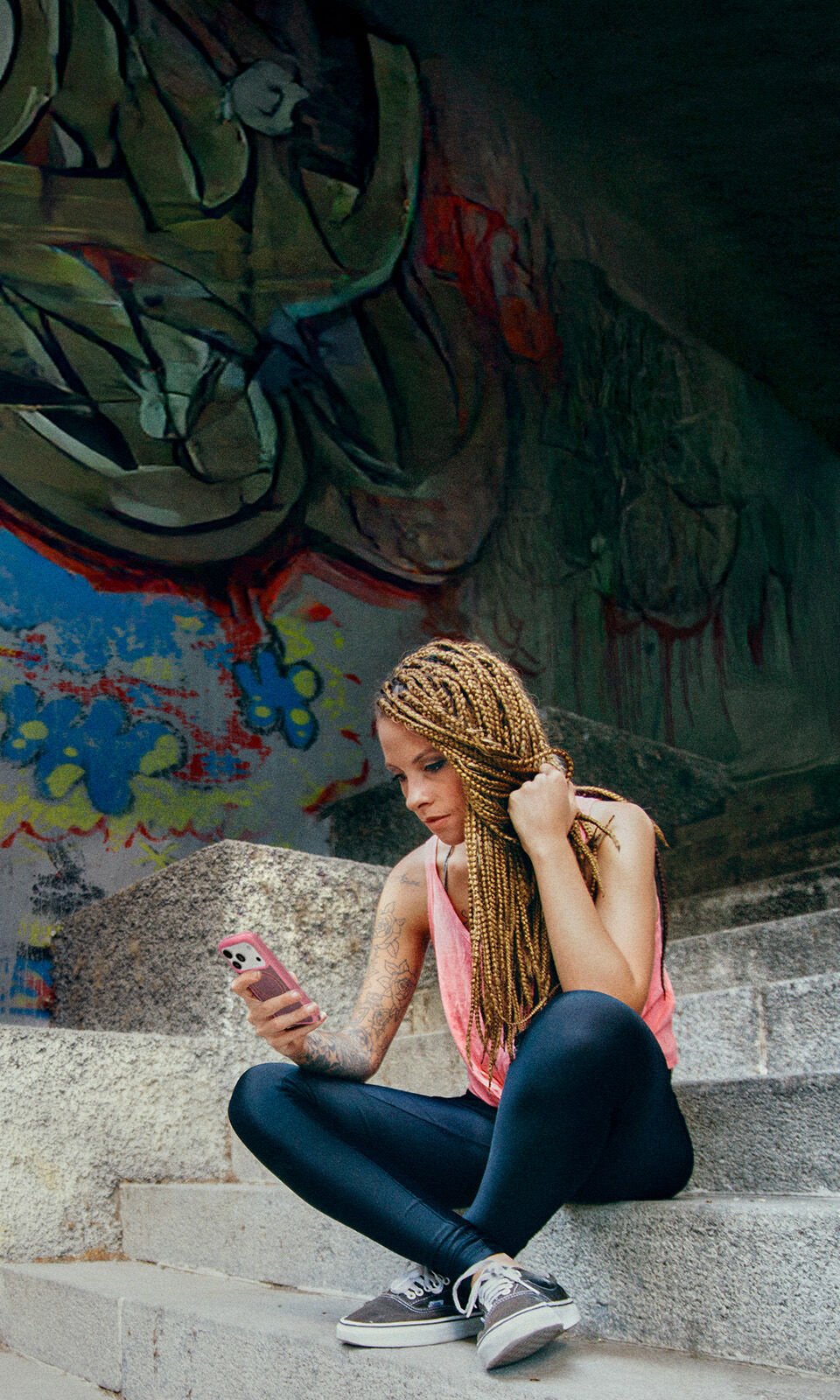 Person sitting on steps using a phone with graffiti in the background
