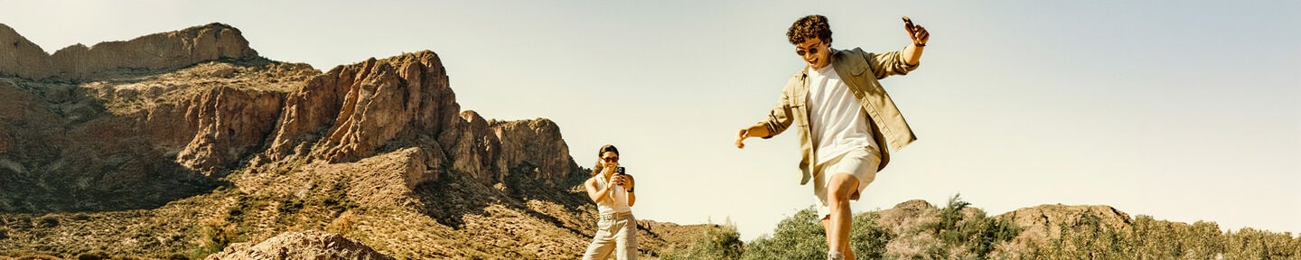 Two people running on a rocky landscape with mountains in the background