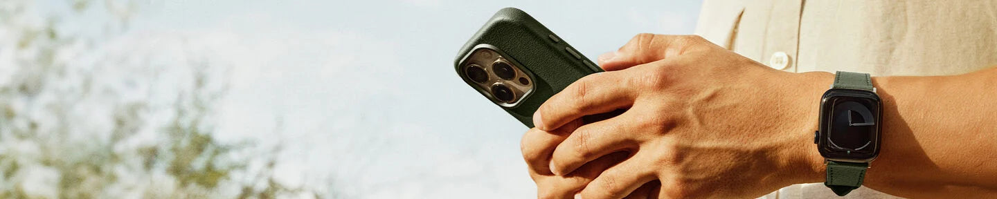 Person holding a smartphone and smartwatch with a blurred natural background
