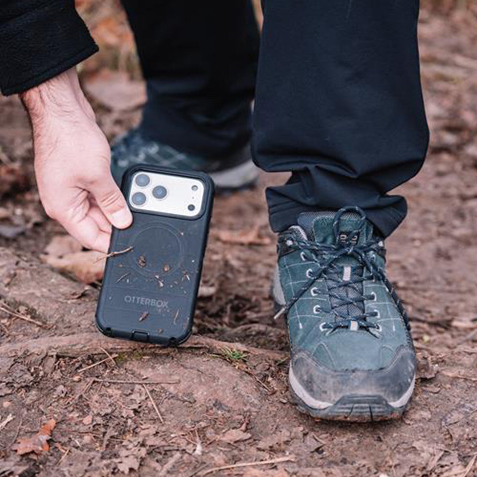 Person holding a phone case with outdoor shoes and pants in the background