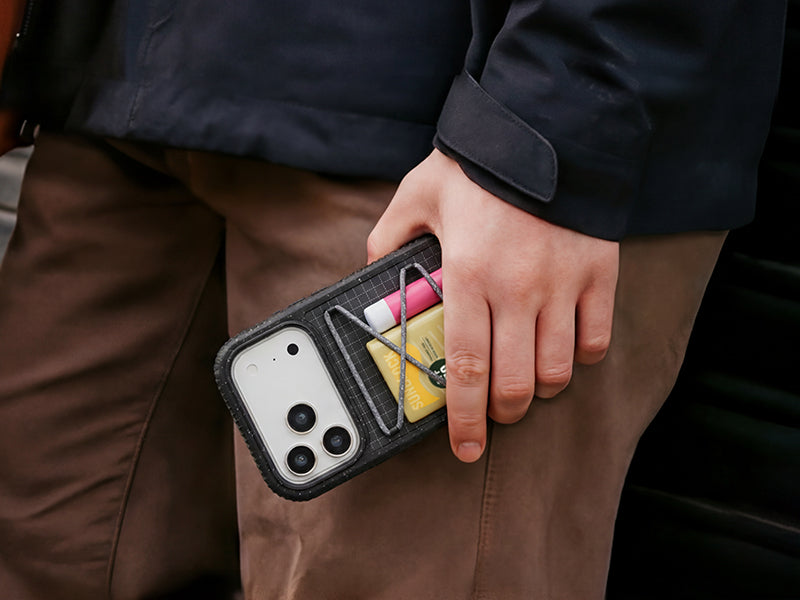 Person holding a phone case with tools inside, wearing a dark jacket and brown pants.