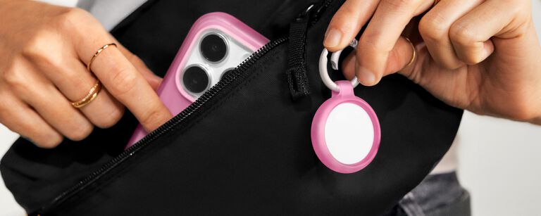 Person holding pink phone and AirTag cases